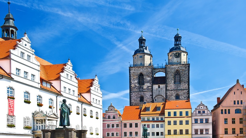 Staty av Luther mot medeltida bebyggelse och en klarbl himmel. i Wittenberg.